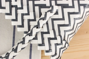 Macro detail of hand-woven plastic stripes and thick braided handles on a black and white tote