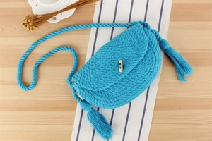 Détail du sac tissé en corde de coton bleu ciel avec bouton en bois et longs glands latéraux