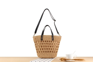 Detail of hollow woven beach tote with black leather straps on a wooden table