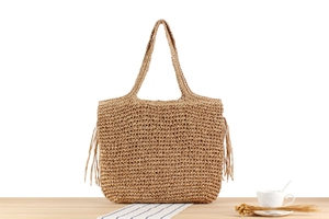 Detail einer handgewebten Strohtasche mit Fransen auf heller Holzoberfläche
