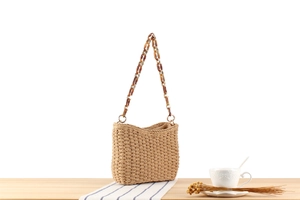 Detail of straw woven bag featuring amber acrylic chain and natural texture finish