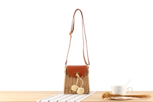 Detail of woven straw bag with brown leather flap, metal lock, and plush ball accents