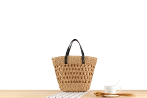 Detail of hand-woven straw tote bag with hollow pattern and black leather handles
