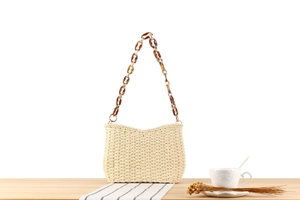 Detail of hand-woven straw bag featuring amber acrylic chain links and golden hardware
