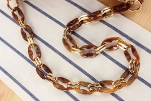 Detail of amber acrylic and gold metal chain strap with spring hooks for shoulder bags