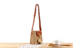 Detail of paper straw crossbody bag with brown leather trim and decorative round balls
