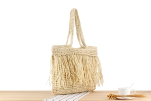 Detail der handgewebten beigen Strohtasche mit langen Fransen auf hellem Holztisch