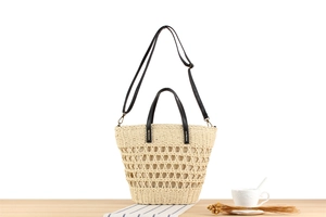 Detail of beige woven tote bag with black leather handles and hollow geometric pattern