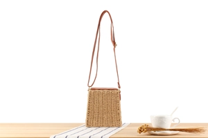 Detail view of woven straw crossbody bag with brown leather strap on wooden surface