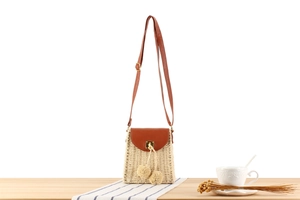 Detail of beige straw crossbody bag with leather flap and decorative pom poms