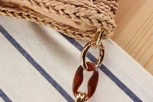 Detail of woven straw bag with amber acrylic chain and gold metal hook attachment