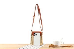 Detail of handwoven paper rope crossbody bag with brown leather flap next to a smartphone