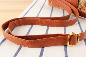 Detail of brown leather strap with gold metal buckle on a woven vintage crossbody bag