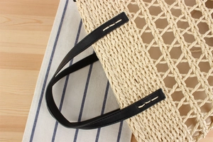 Detail of hollow diamond weave straw bag with black leather handle and white stitching