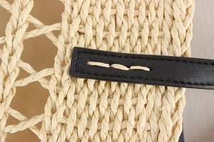 Detail of woven straw handbag featuring black leather strap with white stitching