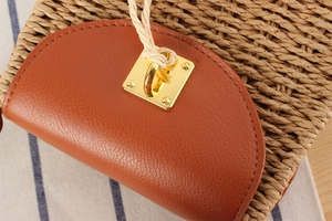 Close-up of woven straw bag with brown leather flap and golden square metal buckle
