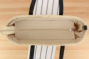 Top view of woven beach tote with beige lining, zipper closure, and black leather handles