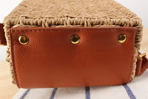 Detailed close-up of woven paper straw bag with leather base and gold metal protective feet
