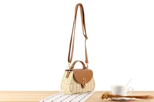 Detail der handgewebten Strohtasche mit brauner Lederklappe, Goldschnalle und Gurt