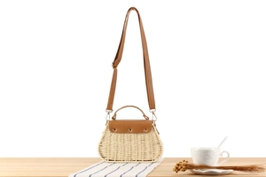 Detail der gewebten Strohtasche mit brauner Lederklappe und Nieten auf Holztisch