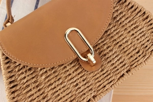 Detail einer Strohhandtasche mit brauner Lederklappe und goldener U-förmiger Metallschnalle