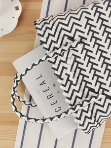 Handwoven striped tote bag with black and white zigzag pattern on a wooden desk