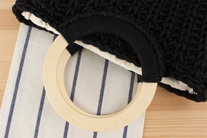 Detail of a black hand-woven cotton bag featuring round wooden handles and linen lining