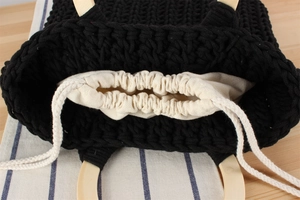 Close-up of black woven cotton tote with round wooden handle and white drawstring liner
