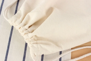 Detail of cream cotton drawstring bag showing woven texture and thick rope closure