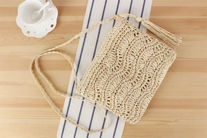 Gros plan du sac bandoulière beige tissé main avec pompons boho sur table bois