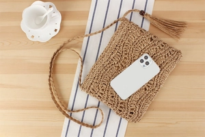 Détail du sac bandoulière en paille tressé à la main avec pompon et téléphone
