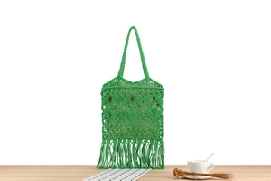 Detail of green macrame woven shoulder bag with intricate diamond patterns and long tassels