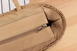 Detail shot of straw tote bag showing smooth metal zipper closure and fabric lining
