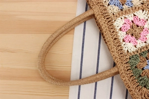Detail of bohemian handmade straw bag with colorful crochet floral patches and handles