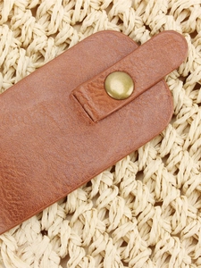 Detailed view of woven straw bag featuring a brown lychee leather strap and gold metal button