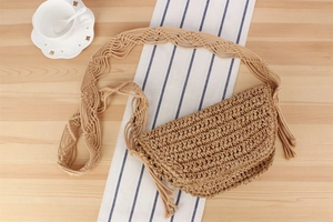 Detail view of woven paper rope crescent bag with macrame strap and tassel on wood surface
