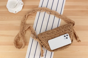 Detail of hand-woven crossbody bag with tassel and patterned strap on a wooden table
