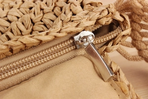 Macro detail of the metal zipper closure and soft lining on the woven straw bag