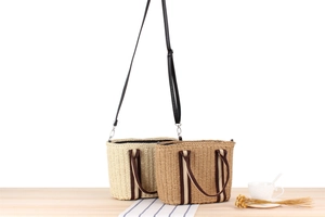 Close-up of woven straw tote bag texture with striped webbing handle on wooden surface