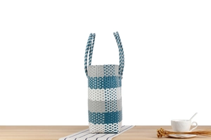 Dettaglio della borsa in plastica intrecciata con strisce bianche e blu sul tavolo