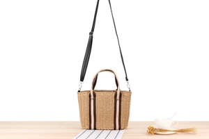 Straw woven tote bag detail with striped fabric handles and leather shoulder strap