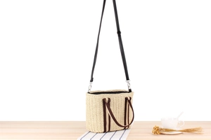 Detail of hand-woven straw tote with striped canvas handles and leather strap on a table