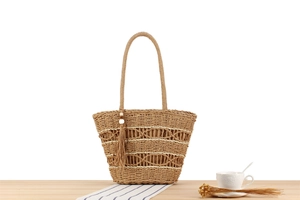 Detail of woven straw tote bag with intricate crochet pattern and fringe tassel ornament