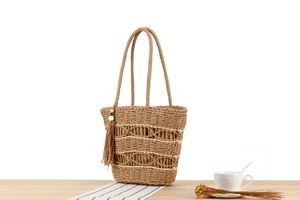 Close-up of woven straw tote bag with delicate openwork pattern and fringe tassel detail