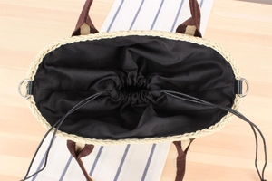 Top view of woven straw tote bag with brown handles and black drawstring inner lining