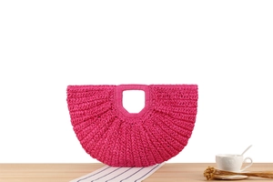 Detail of hand-woven rose pink crescent handbag with integrated handle on wooden surface