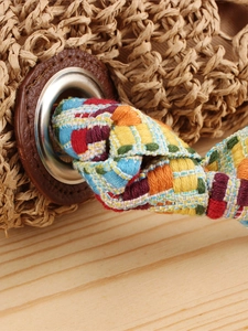 Vintage handwoven straw shoulder bag with colorful jacquard strap on a wooden surface