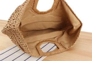 Detail view of woven straw tote bag featuring beige fabric lining and dual interior zip pockets