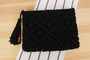 Detail of black macrame cotton rope envelope clutch featuring boho fringes and metal rings