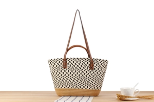 Detail of woven tote bag with geometric patterns and leather handles on wooden table
